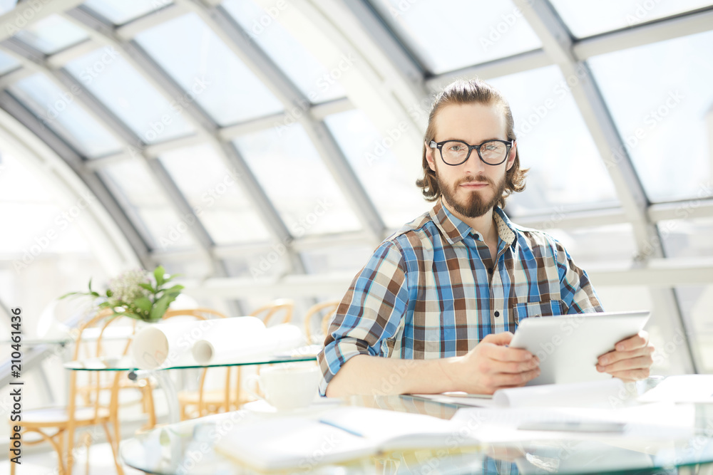 Young serious businessman with touchpad looking at you while searching for new trends in the net Young serious businessman with touchpad looking at you while searching for new trends in the net