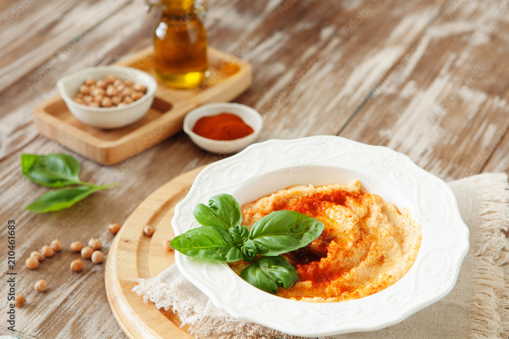 Fresh classic hummus with basil in the bowl on wooden background