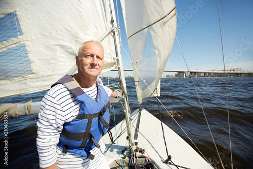 Senior man in lifejacket sitting in yacht and enjoying summer weekend by seaside