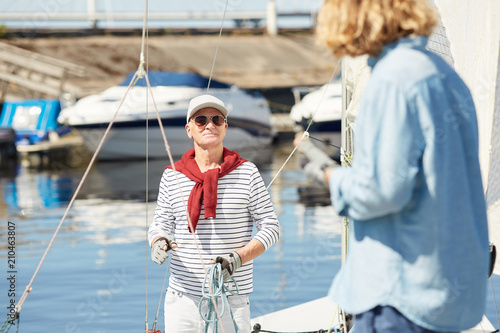 Senior man in sunglasses talking to his assistant while preparing yacht for sailing