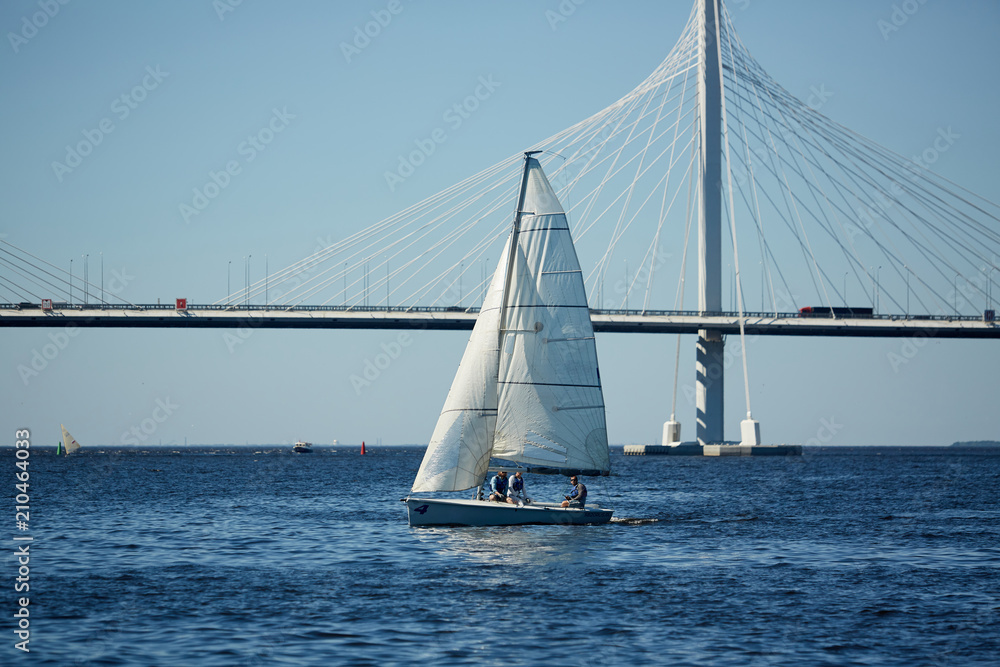 Group of humans in yacht sailing in large sea with bridge on background and blue sky above