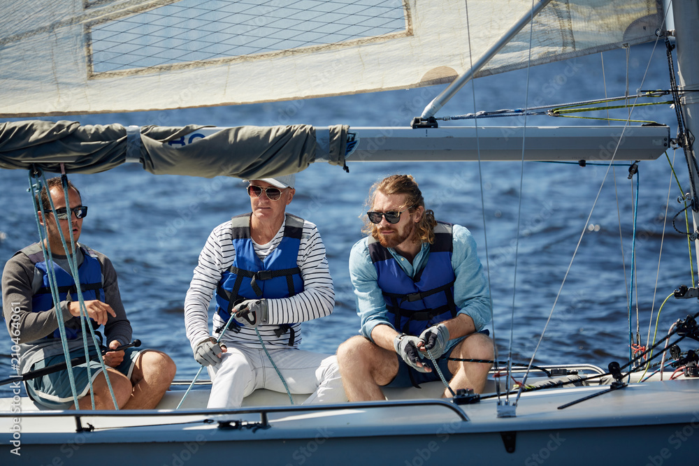 Fototapeta premium Team of three active men in lifejackets sitting in yacht while sailing in the sea