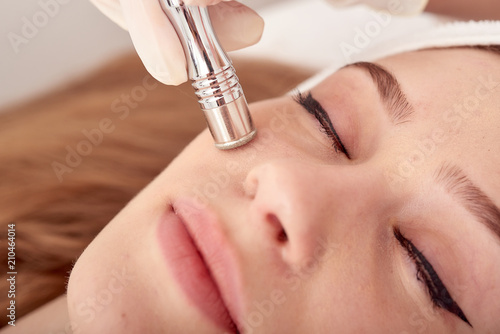 The cosmetologist makes the procedure Microdermabrasion of the facial skin of a beautiful, young woman in a beauty salon.Cosmetology and professional skin care. photo
