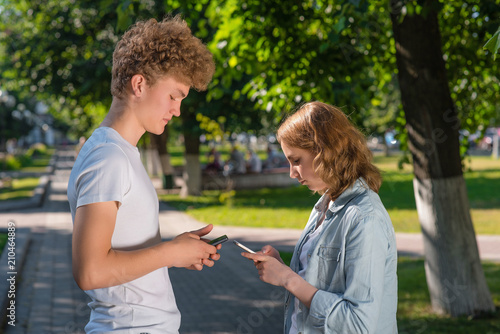The boy and girl are facing each other. Summer in nature. In his hands holds a smartphone. Writes the phone number. Emotion dating in the park. . The guy gets acquainted with the girl. © byswat