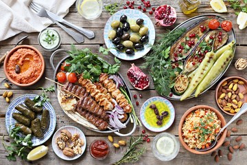 Middle eastern, arabic or mediterranean dinner table with grilled lamb kebab, chicken skewers  with roasted vegetables and appetizers variety serving on wooden outdoor table. Overhead view.