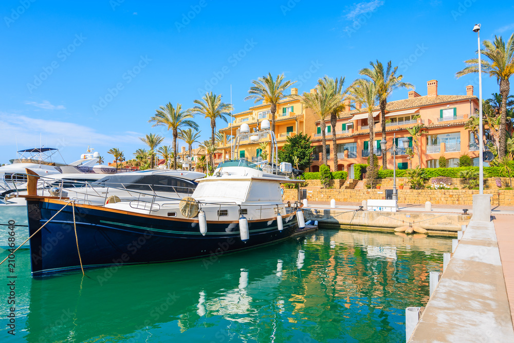 Boat anchoring in Sotogrande marina with colorful houses, Andalusia, Spain