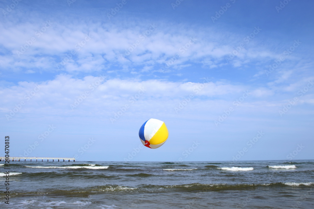 Colorful beach ball in flight over sea. Holiday beach ball in the sky on sea background.