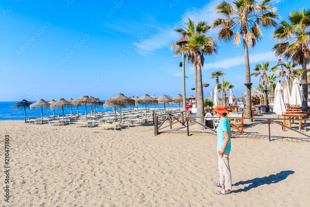 Young woman tourist standing on beautiful beach with palm trees near Marbella, Andalusia, Spain