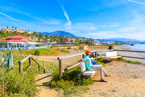 Young woman tourist sitting on bench and looking at beach near Estepona town on Costa del Sol, Spain