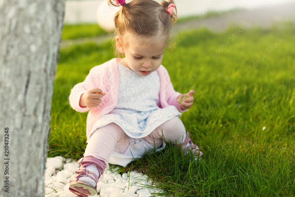 little curly girl with two tails sitting on a lawn near a tree little curly girl with two tails sitting on a lawn near a tree