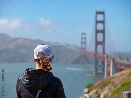 Rearview of woman in baseball cap looking out at Golden Gate Bridge and Marin Headlands