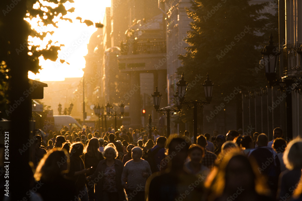 Silhouette crowd of people walking down the pedestrian zone at summer evening sunset