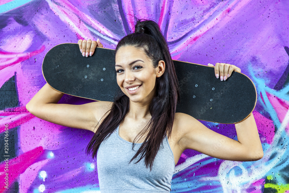 Fototapeta premium Young fit beautiful girl sitting outdoor with skateboard on her shoulders