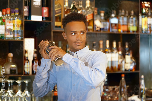  Bartender man holding in hands a shaker with a fresh delicious cocktail. Bartender shaking a cocktail shaker as she stands behind the bar mixing a drink for a client. Close-up.