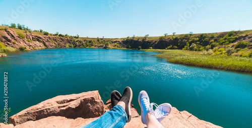 Travelers couple in sports shoes on a mountain near a river in the background of nature. Man and woman. A couple sits and makes their feet on a beautiful landscape with a river bank summer