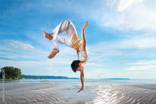 A young guy trains capoeira on the beach.