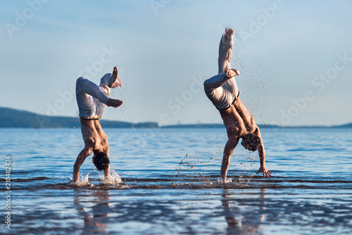 The man is a coach of capoeira and a boy practicing capoeira on the beach. Man and young guy play staged fight.