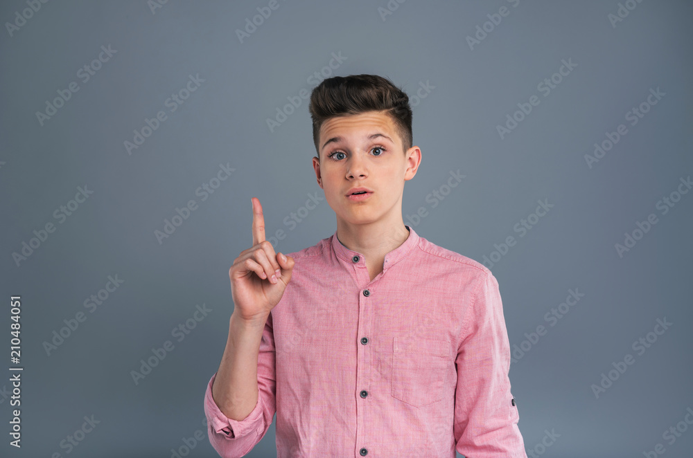 Have an idea. Charming teenage boy having a fresh idea and raising his index finger to indicate it while posing isolated on a blue-grey background Have an idea. Charming teenage boy having a fresh idea and raising his index finger to indicate it while posing isolated on a blue-grey background