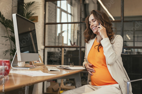 Good news. Low angle of exuberant pregnant CEO talking on phone and laughing photo