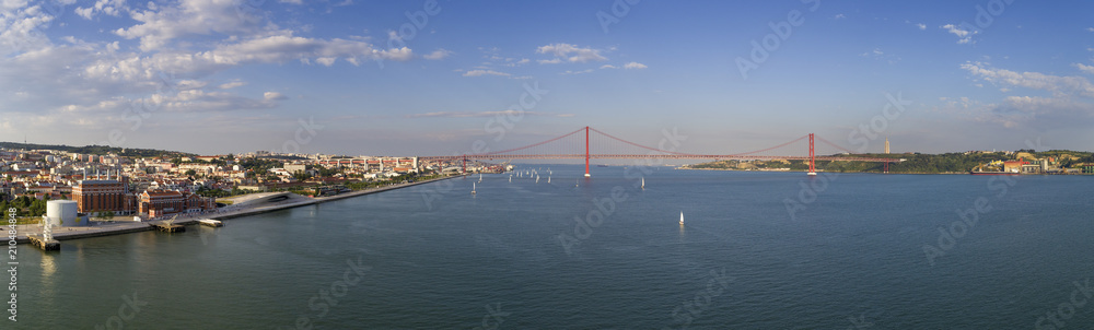 Aerial panoramic view of the city of Lisbon with sail boats on the Tagus River and the 25 of April Bridge (Ponte 25 de Abril) on the background; Concept for travel in Portugal and visit Lisbon