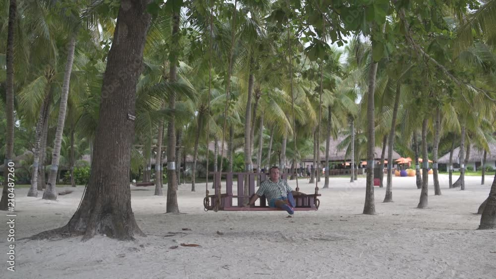 A man swinging on a swing in the street among palms A man swinging on a swing in the street among palms