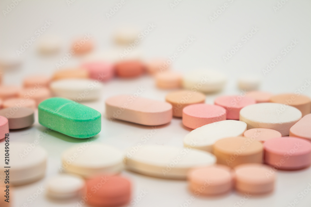 Multiple white and pink and green pills on a white background with several of them out of focus. Medications in the form of tablets. Multiple white and pink and green pills on a white background with several of them out of focus. Medications in the form of tablets.
