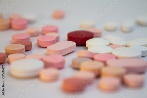 Multiple white and pink and red pills on a white background with several of them out of focus. Medications in the form of tablets.