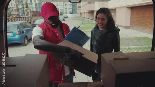 Courier African American gives a parce to a woman after signing on delivery device cardboard technology box order post postal service device sunny beard covered load logistic mailman photo