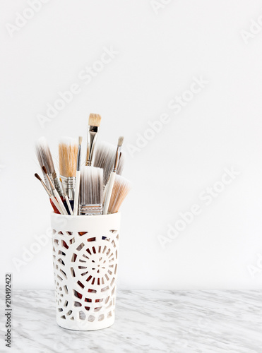 Paintbrushes in a decorative vase on marble surface