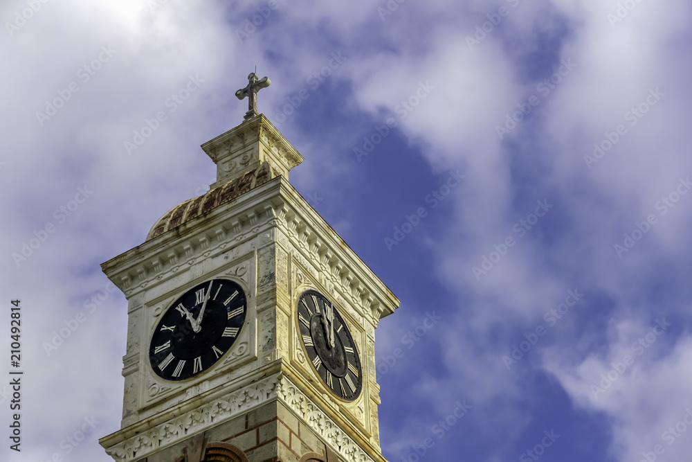 An ancient clock tower of the monastery with a cross on a background of a bright blue sky and clouds