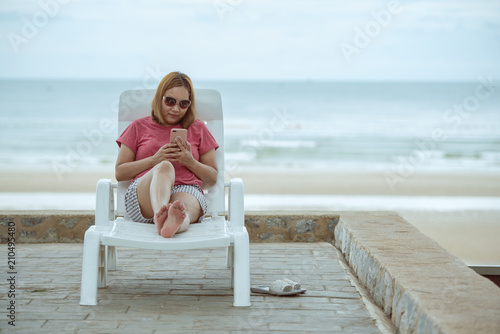 Young woman sitting on the beach chair and using mobile phone.
