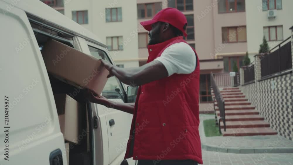 Happy courier African American young man takes the box out of the car and goes smile portrait cardboard technology box order post postal service device sunny beard covered load logistic mailman Happy courier African American young man takes the box out of the car and goes smile portrait cardboard technology box order post postal service device sunny beard covered load logistic mailman