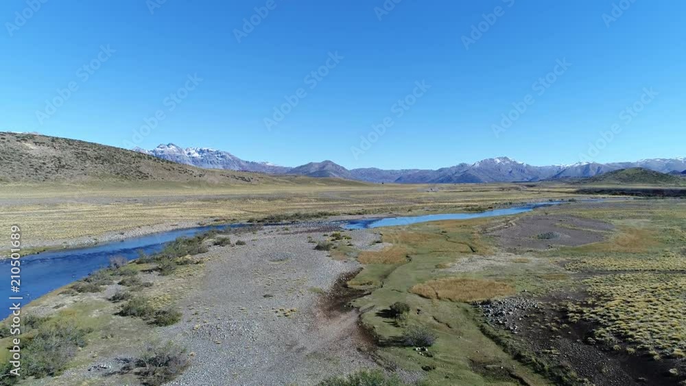Aerial drone scene of estepa and Nahueve river in north neuquen, Patagonia Argentina. Camera moving upwards on sunny day. Andes mountains with snow at the background. Epu Lauquen lakes. Aerial drone scene of estepa and Nahueve river in north neuquen, Patagonia Argentina. Camera moving upwards on sunny day. Andes mountains with snow at the background. Epu Lauquen lakes.
