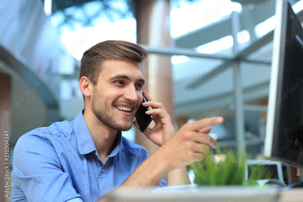 Smiling businessman sitting and using mobile phone in office. Smiling businessman sitting and using mobile phone in office.