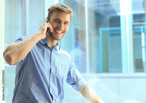 Smiling businessman standing and using mobile phone in office. photo