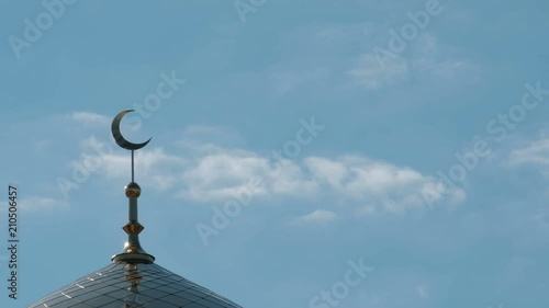 The bird flies by the side of the crescent on the minaret. A close-up of the clouds moving past the top of the Moslem mosque. photo
