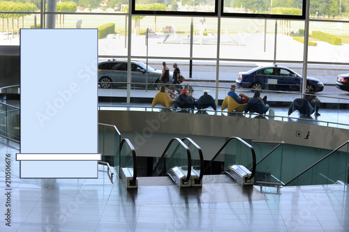 Banr reklamowy, ludzie w szklanej galeri portu lotniczego w pobliżu ruchomych schodów.