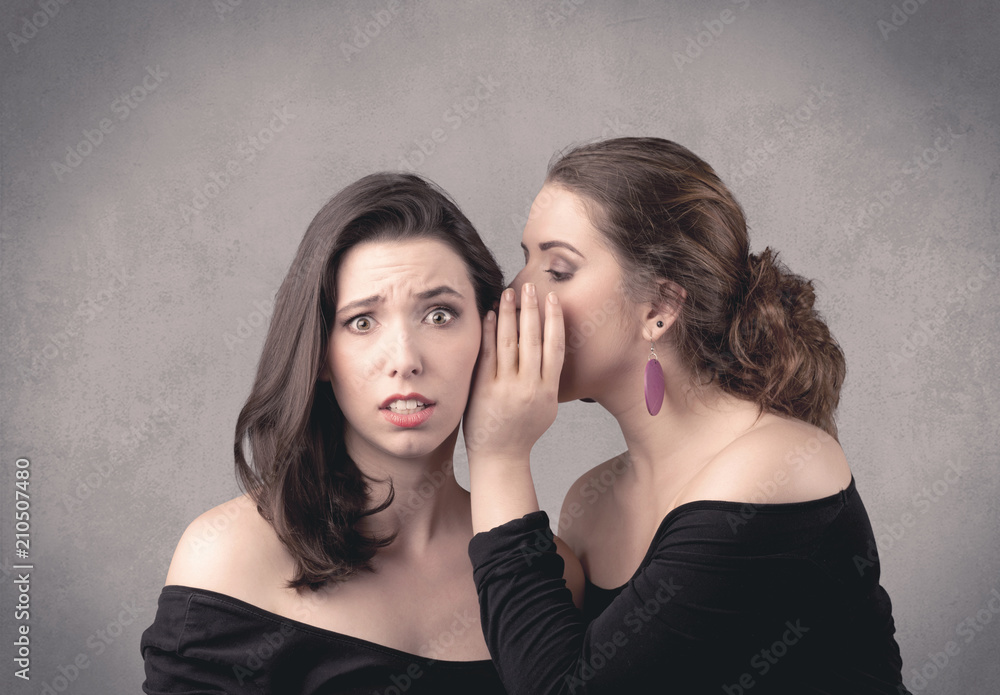 Two fancy dressed actress girls with long hair and make up whispering in front of grey urban background concept. Two fancy dressed actress girls with long hair and make up whispering in front of grey urban background concept.
