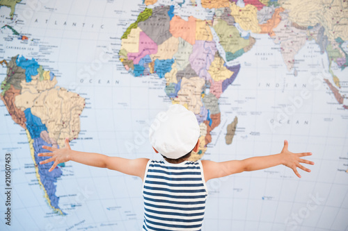 little child in captain hat spreading hands to world map before travel