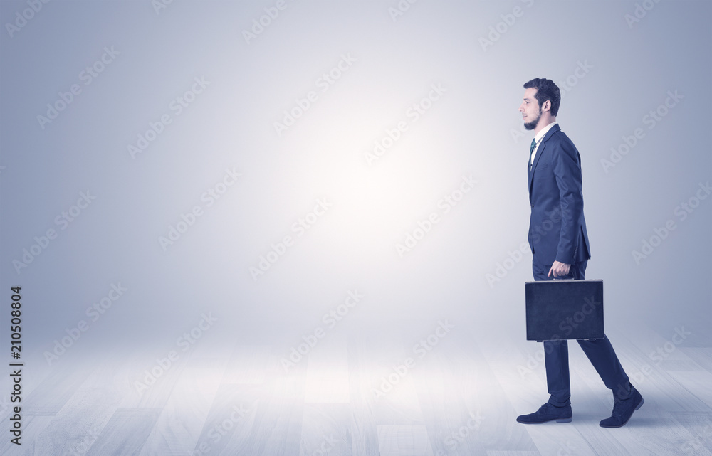 Fototapeta premium Successful businessman walking in front of an empty wall with briefcase on his hand 