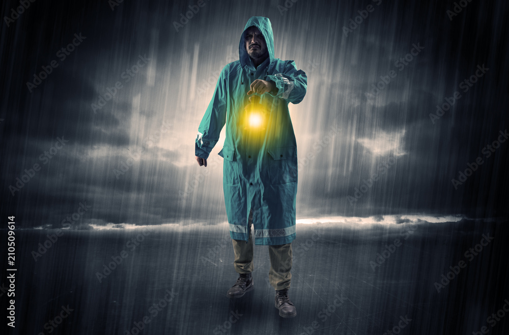 Raincoated man walking in storm with glowing lantern in his hand
