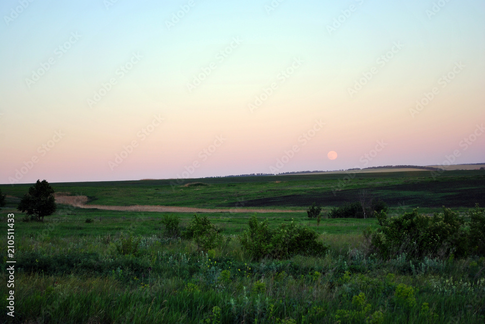 Field on horizon, blue sky and harvest moon rising, Ukraine in spring