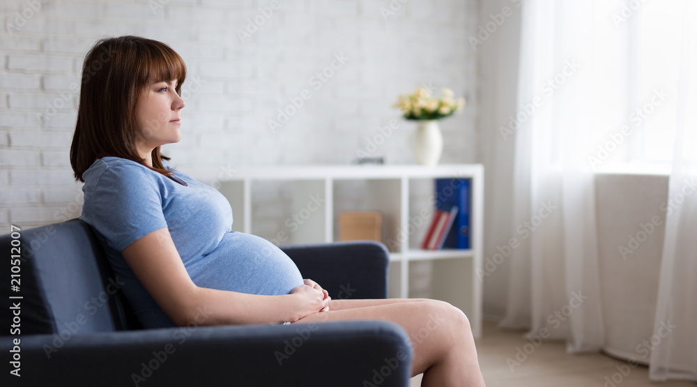 thoughtful pregnant woman sitting on sofa in living room thoughtful pregnant woman sitting on sofa in living room