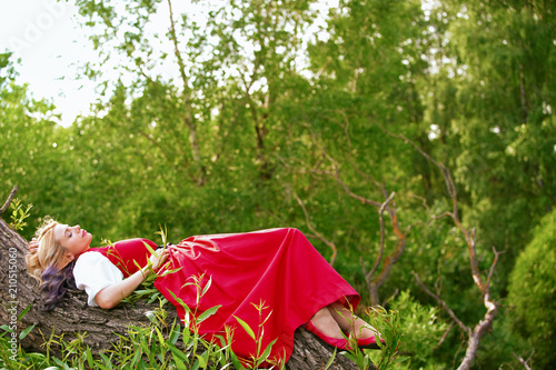 the girl is resting on a tree branch, in a red dress and a white blouse.