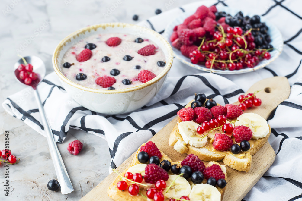 A table with a healthy summer breakfast - oatmeal with berries, currants and raspberries, and a sandwich with peanut butter, banana and various berries