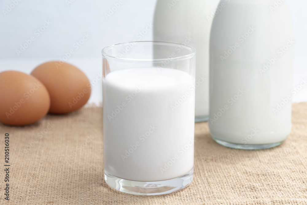 Two glass bottle and a cup of milk with egg on the sackcloth in the blue background for food and healthy concept. with copy space for text. Two glass bottle and a cup of milk with egg on the sackcloth in the blue background for food and healthy concept. with copy space for text.