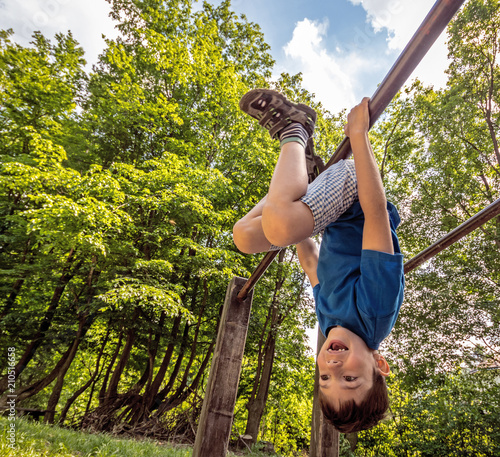 Εκτύπωση καμβά Happy child boy hanging upside  down on bar, playground in forest, outdoor activ