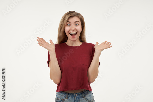 Portrait of surprised woman with wiretap eyes and mouth wide open feeling shocked. Beautiful young woman in casual t-shirt looking at camera in Studio