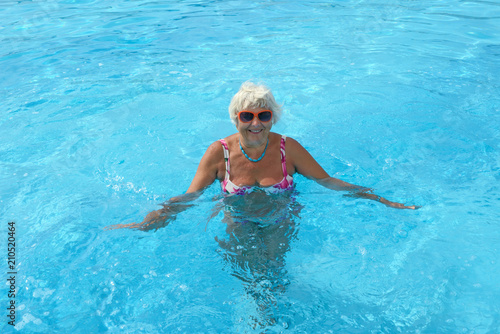 Aged woman is standing in bright blue pool water.