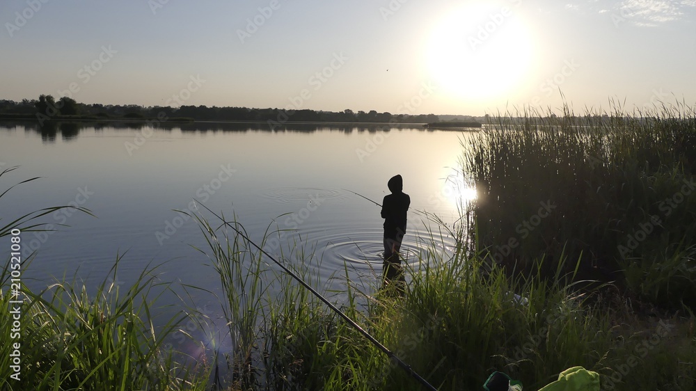 A man with a fishing rod on the shore of the lake is catching fish.